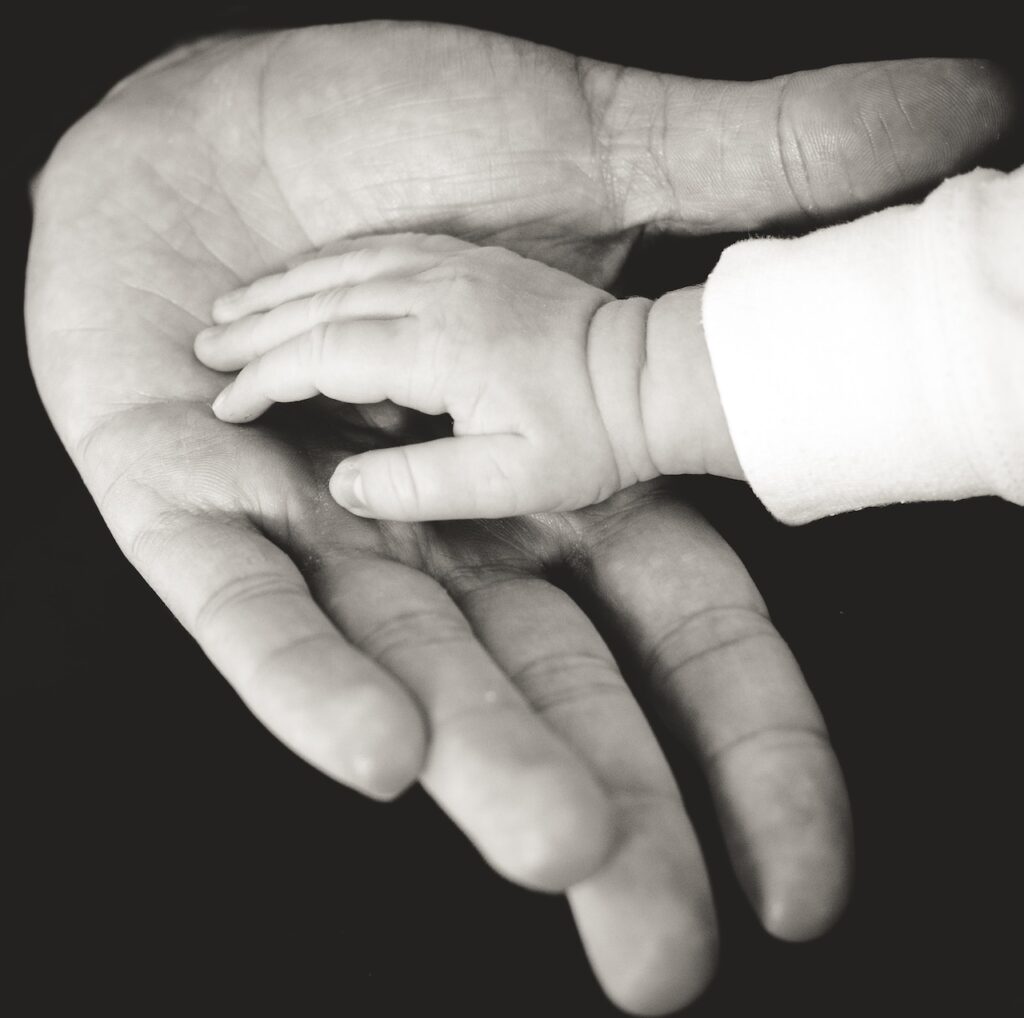 Mano de bebé sobre mano de hombre, a penas se rozan, en blanco y negro.