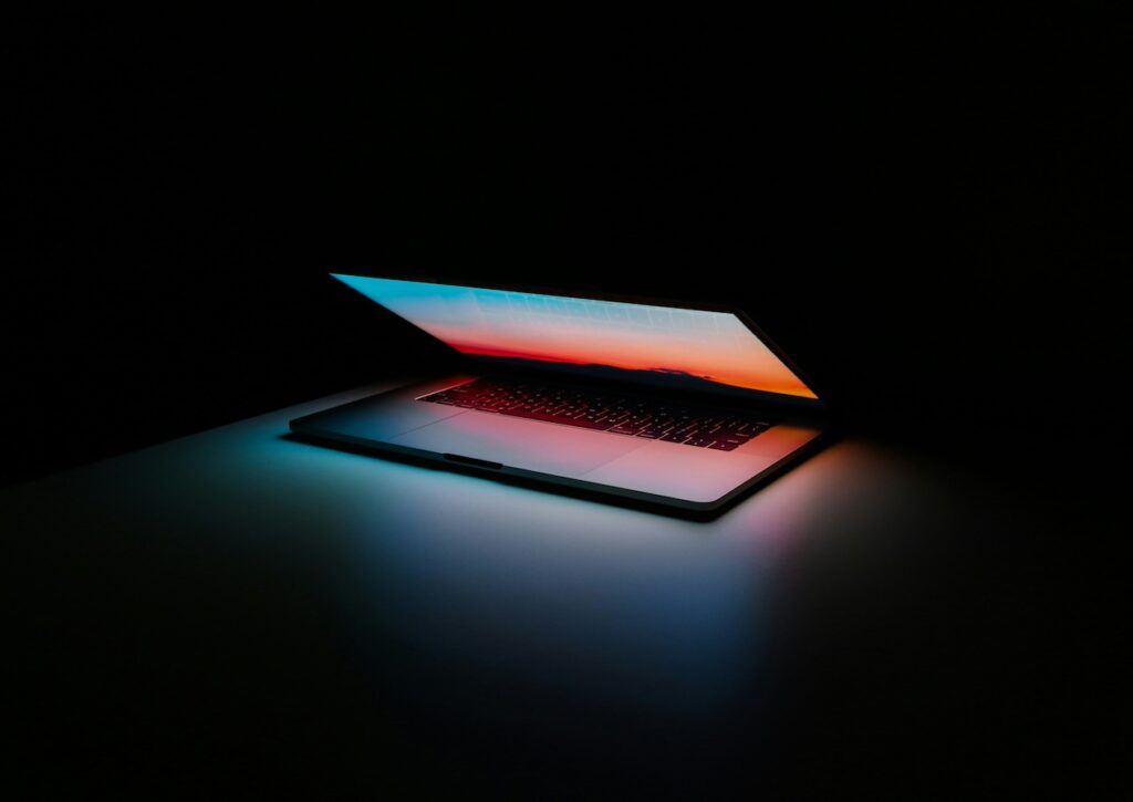 Imagen de una laptop a medio cerrar con la pantalla encendida, en un fondo negro.