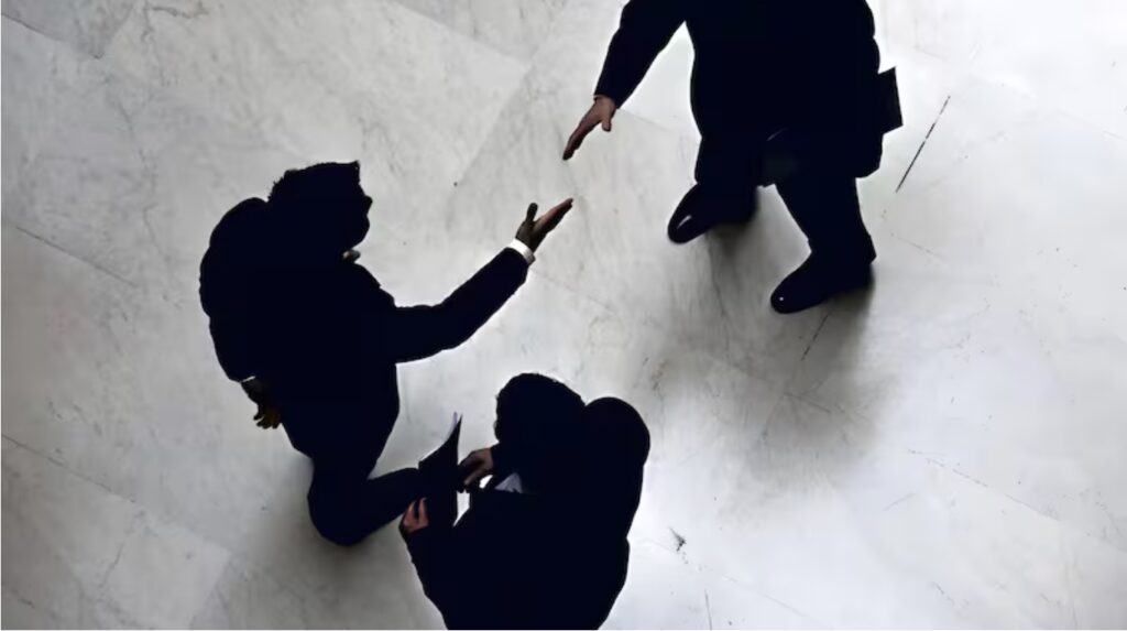 Foto de tres hombres, mirados desde arriba, y dos se acercan a estrecharse la mano.